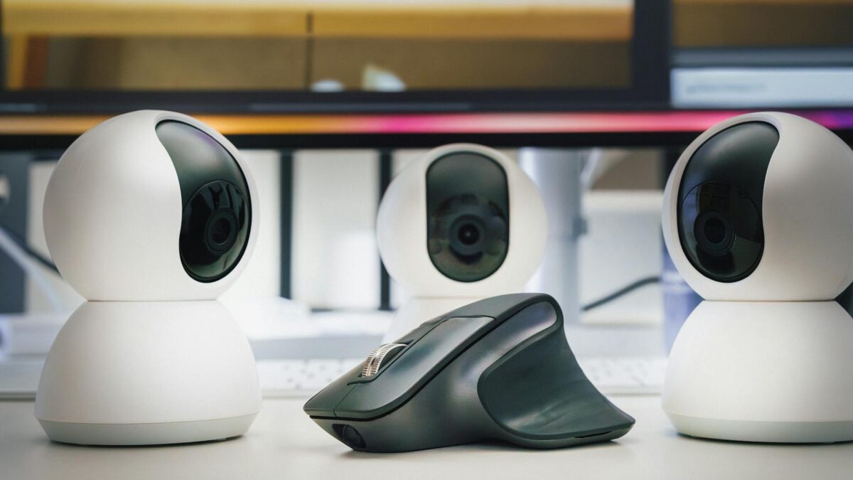 Tres webcams brancas e um mouse sobre mesa de escritorio, demonstrando perifericos modernos para home office e streaming em 2026