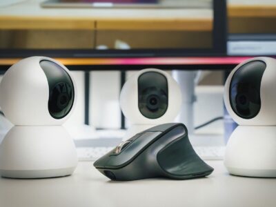 Tres webcams brancas e um mouse sobre mesa de escritorio, demonstrando perifericos modernos para home office e streaming em 2026