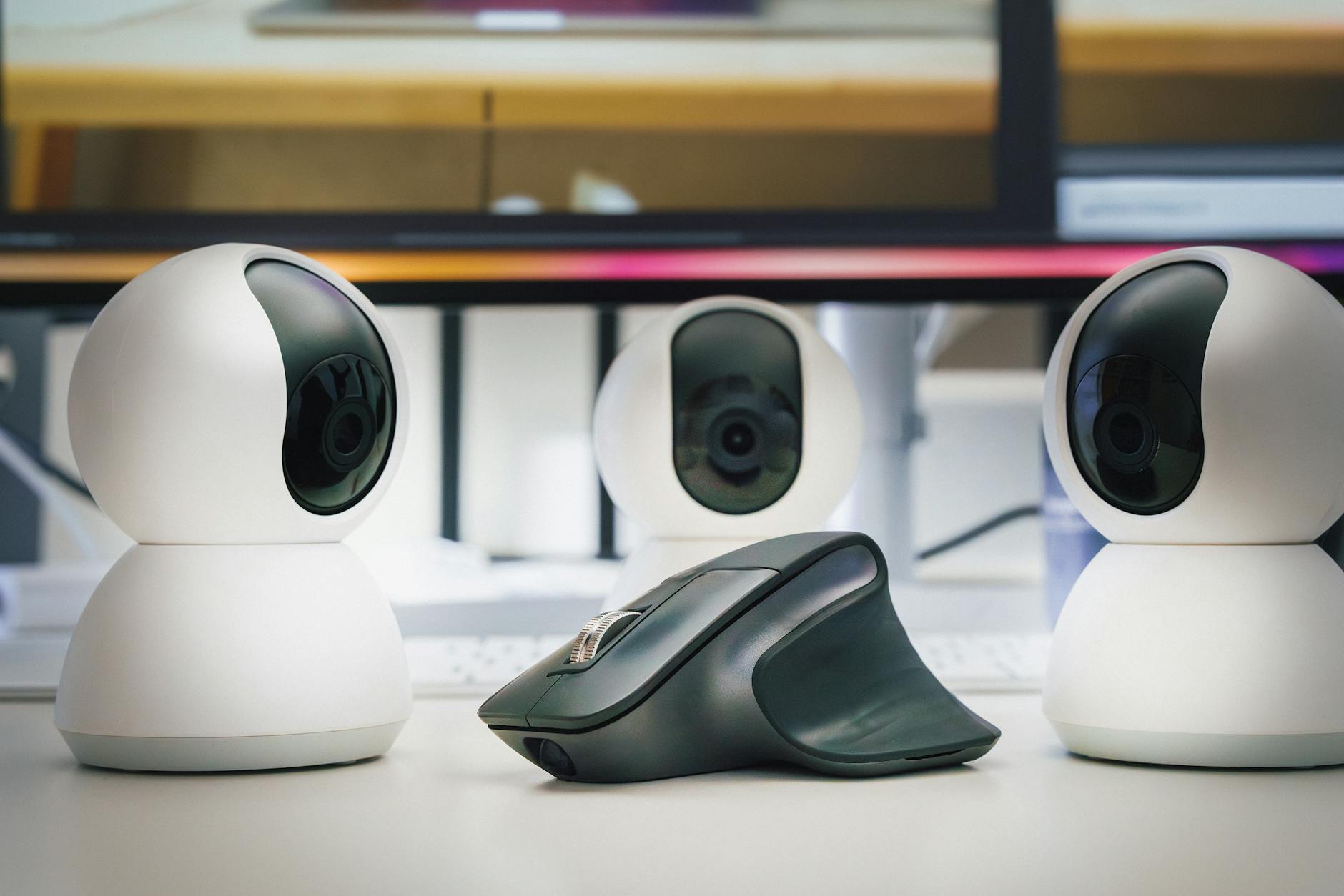 Tres webcams brancas e um mouse sobre mesa de escritorio, demonstrando perifericos modernos para home office e streaming em 2026